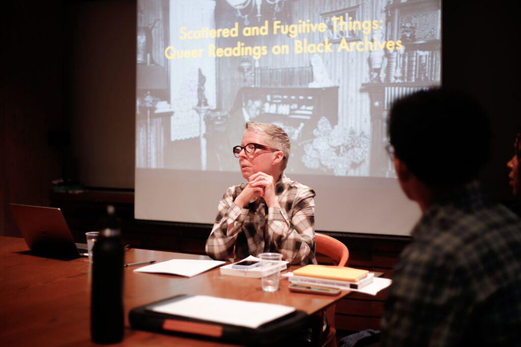 Image of Helton sitting at seminar table in front of slideshow.